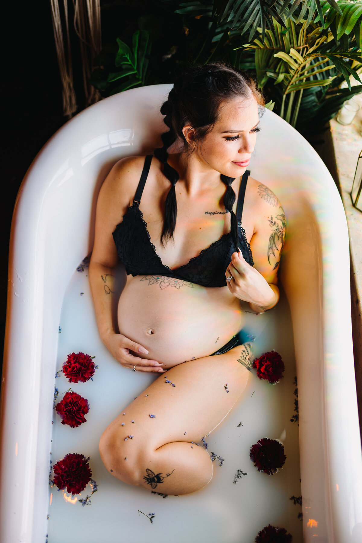 The elegance and serenity of maternity with top Albuquerque photographers. This stunning image features a pregnant woman gracefully posing in a bathtub filled with water and adorned with red roses, highlighting the beauty and anticipation of expecting a new baby.