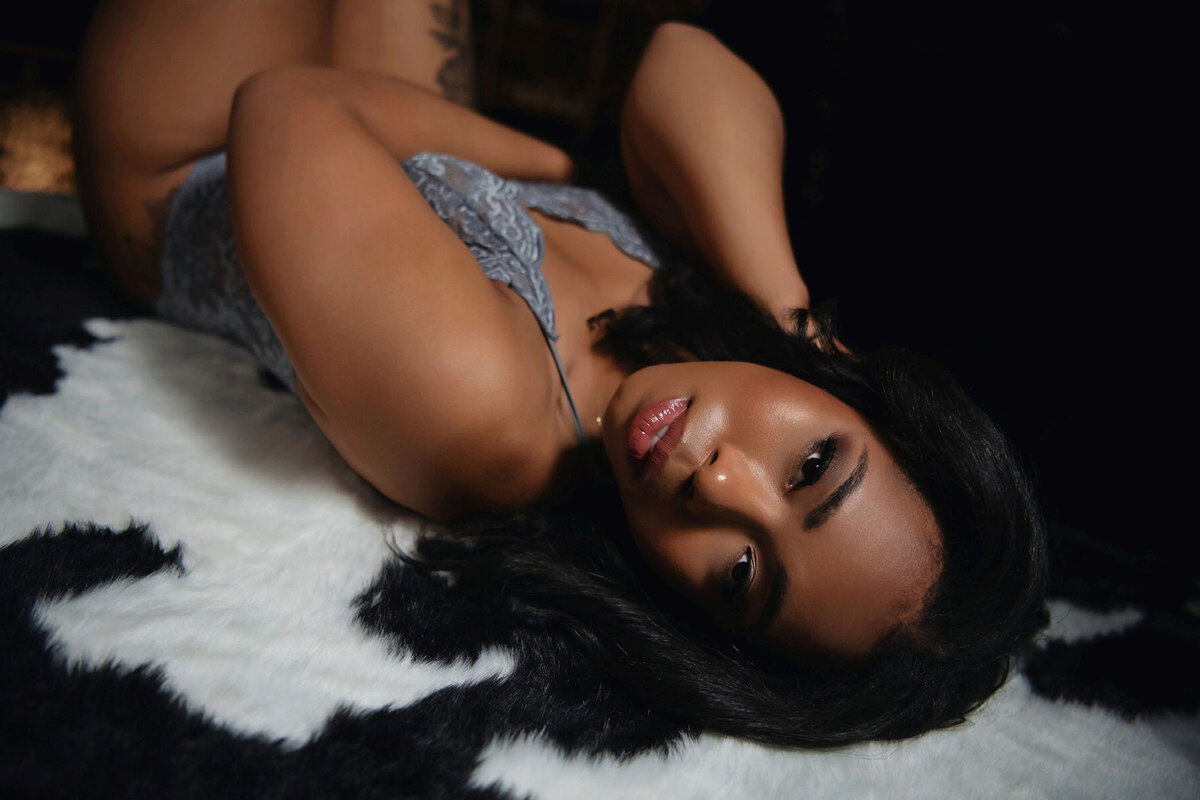 Darkly lit portrait of dark skinned woman posing on cow print rug for boudoir photo