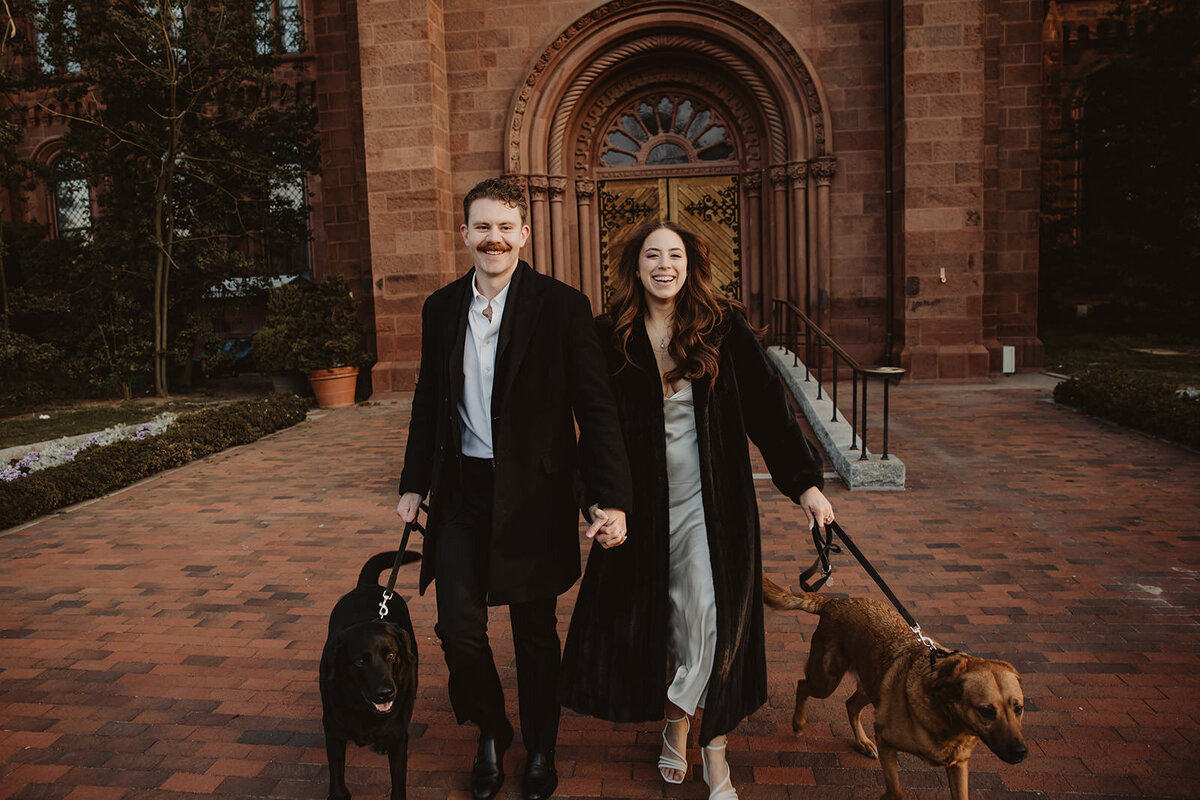 A couple walking together each holding a dog's leash 