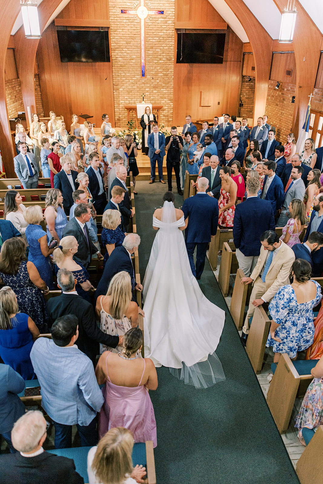 Overhead view of bride walking down church aisle with her father surrounded by wedding guests. 