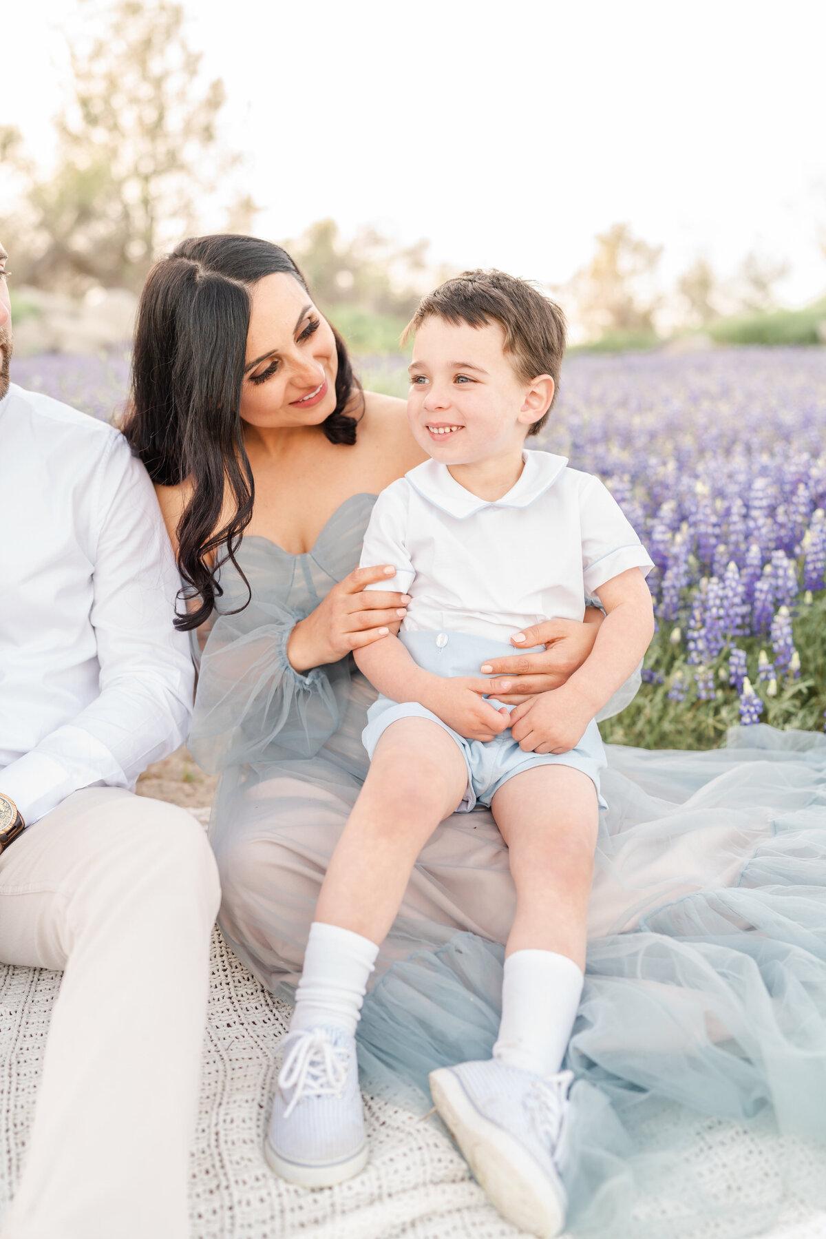 A mother and son sit together in a field of lupines while the mother looks lovingly at her son who is smiling photographed by bay area photographer, Light Livin Photography.