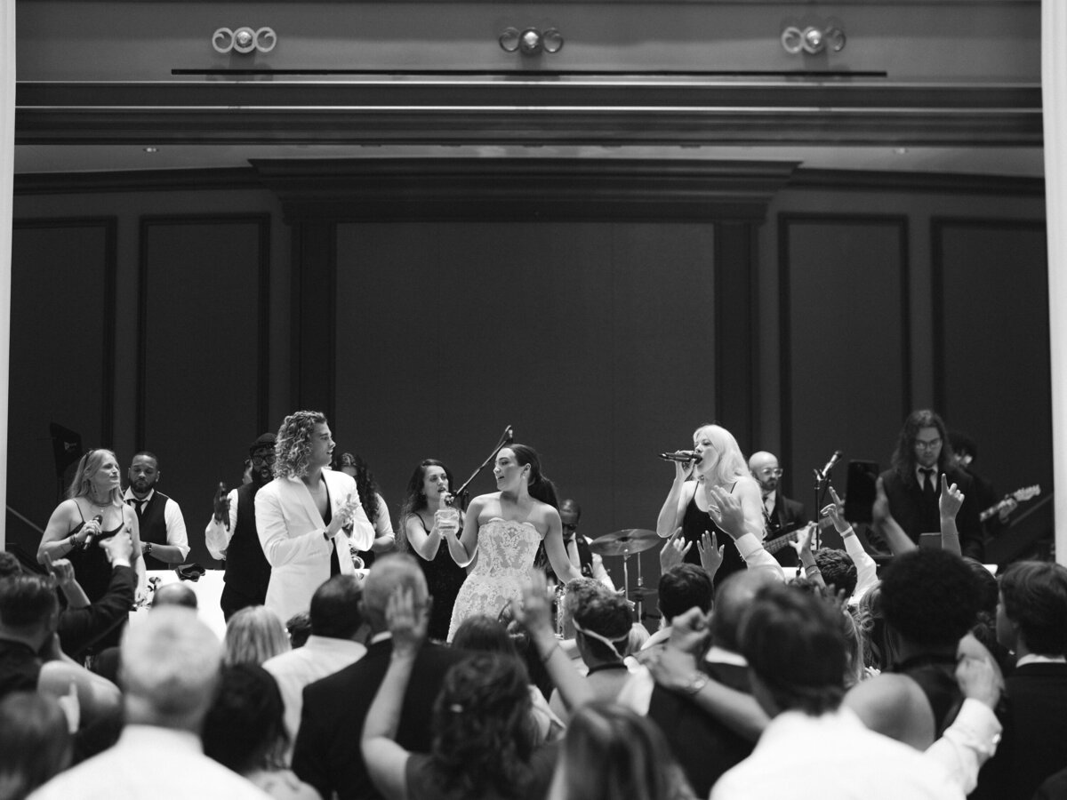 Bride and groom on stage dancing with wedding band at all white luxury wedding reception