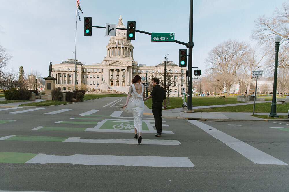 A cinematic shot of a couple running across a crosswalk outside of the Boise ID capitol building.