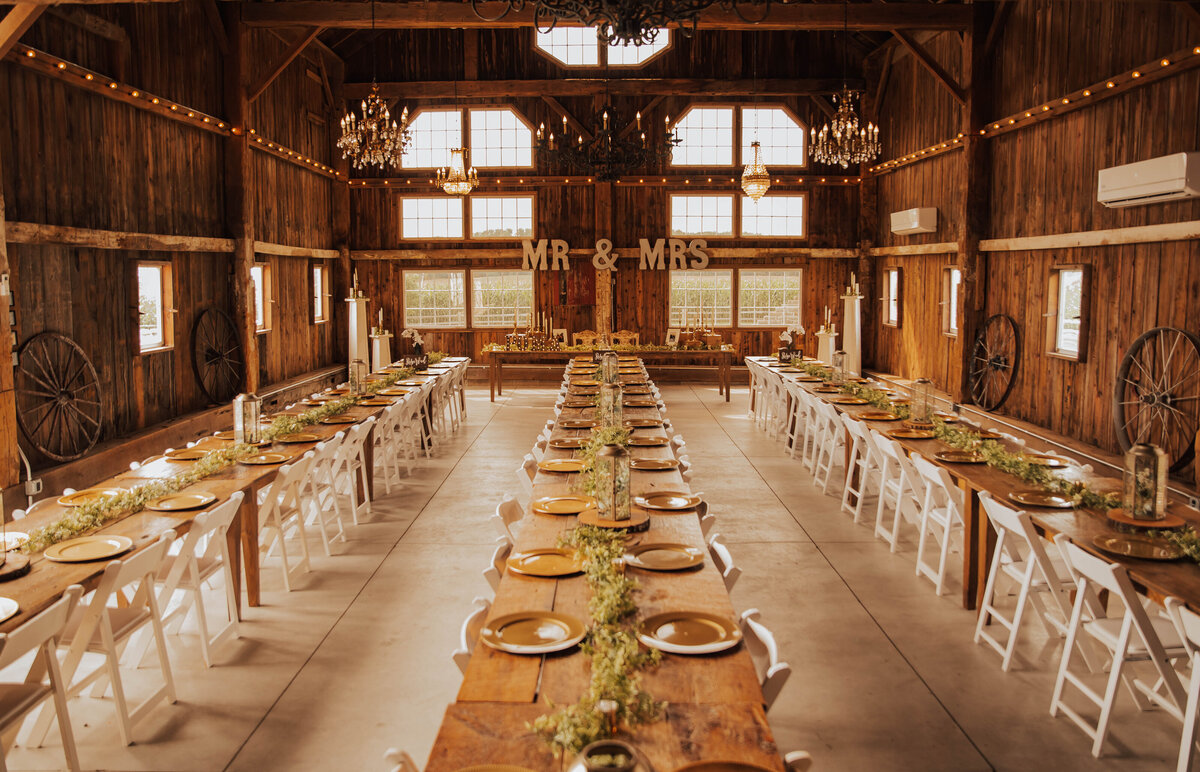 barn wedding venue reception space with long dinner tables and chandeliers
