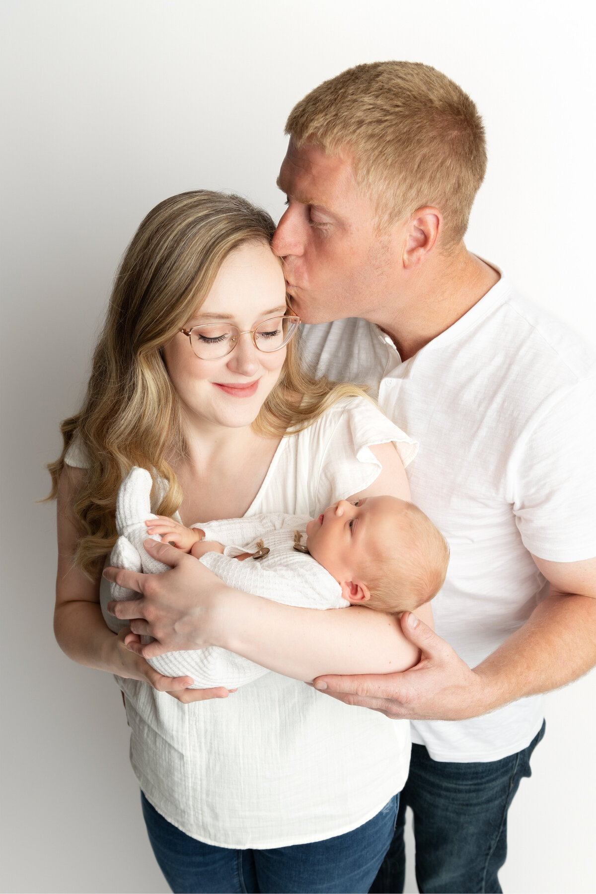 Mother holding newborn son while father kisses her forehead during a newborn family photo in studio in Paris, Ontario