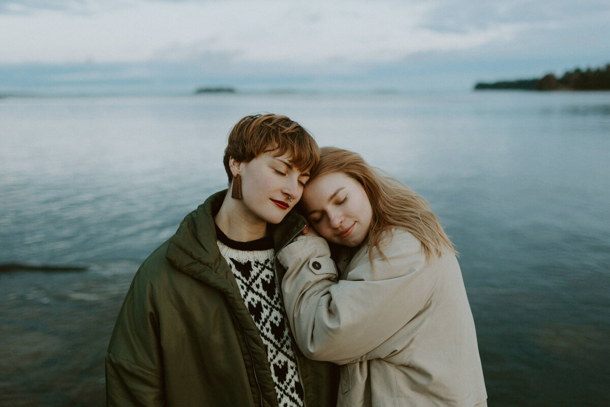Two adult sisters standing by the sea leaning to each other eyes  closed in Helsinki in Finland