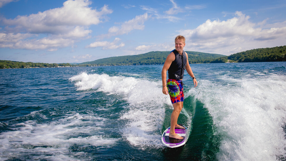 Penn Yan senior boy wakesurfing for his senior pictures on Keuka Lake with a beautiful blue sky