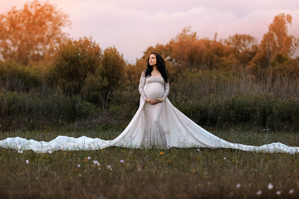 Gorgeous expectant momma looking up while holding her belly while wearing a long dress in Pearland, Texas.