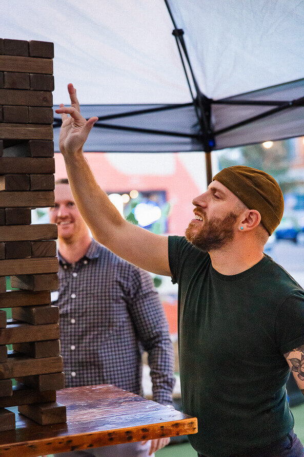 Man with hat taps a giant Jenga block.