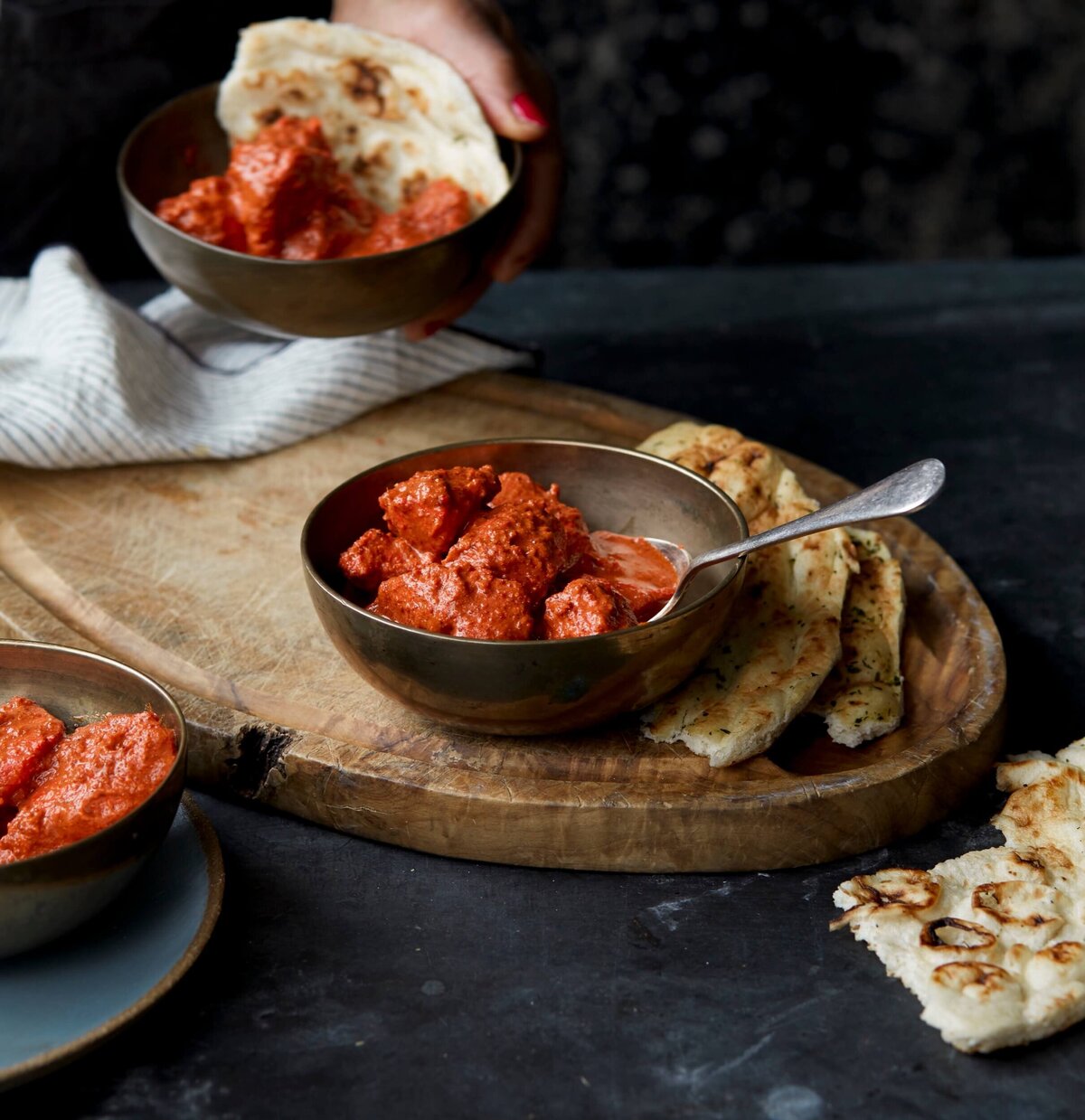 Tandoori chicken in a metal bowl with some naan on the side