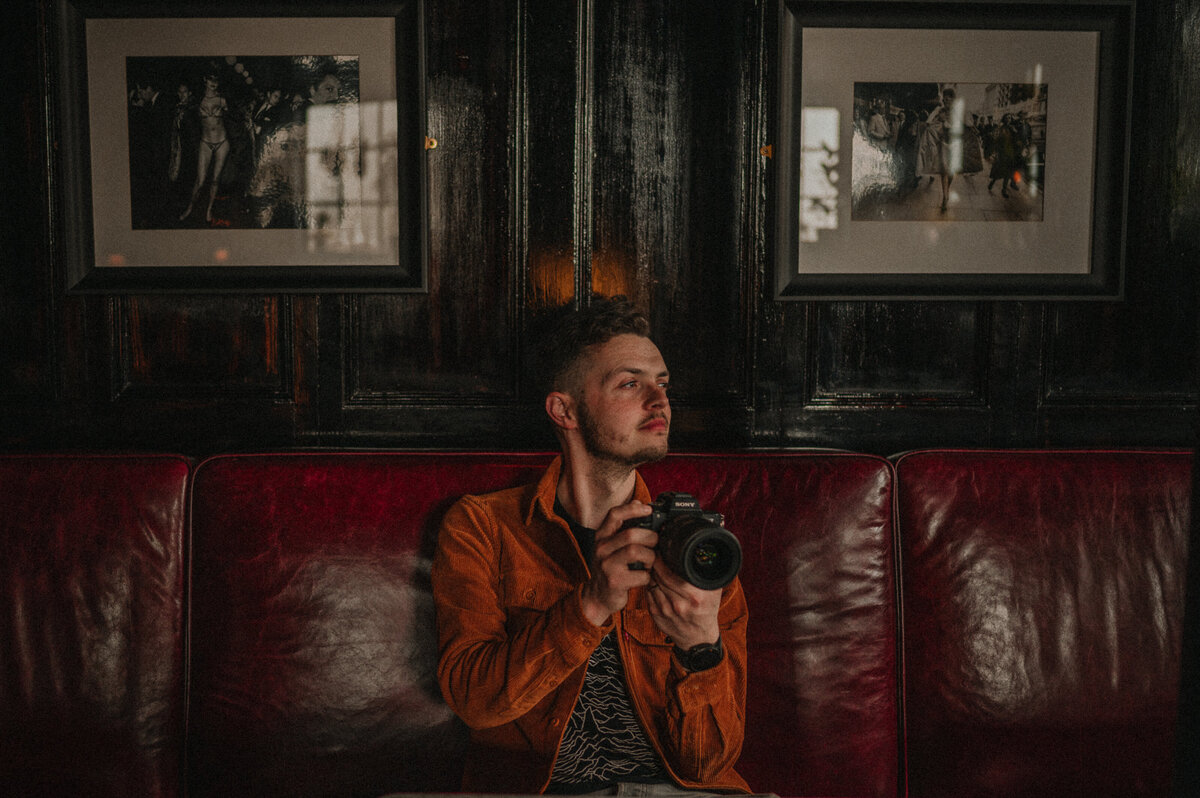 London wedding photographer sits with his camera on a red sofa