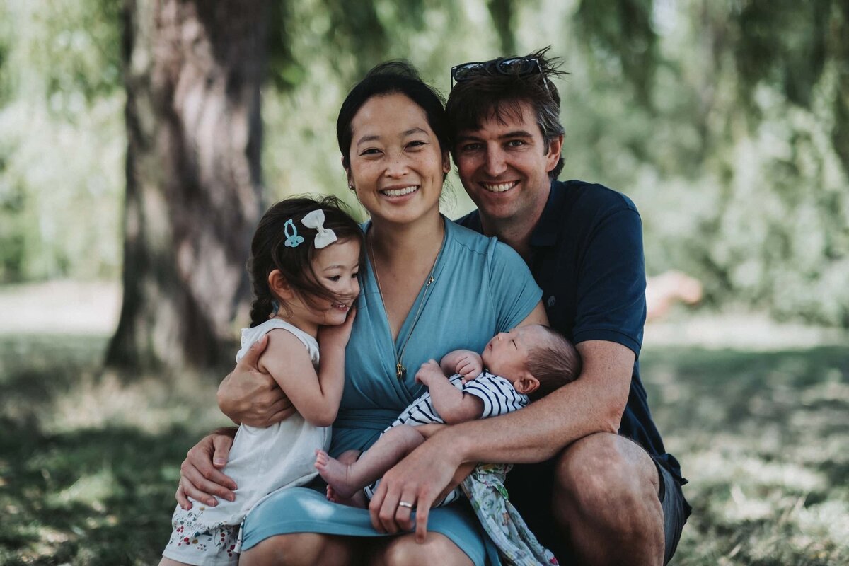 Family of four with newborn baby smiles outside in a Park in London