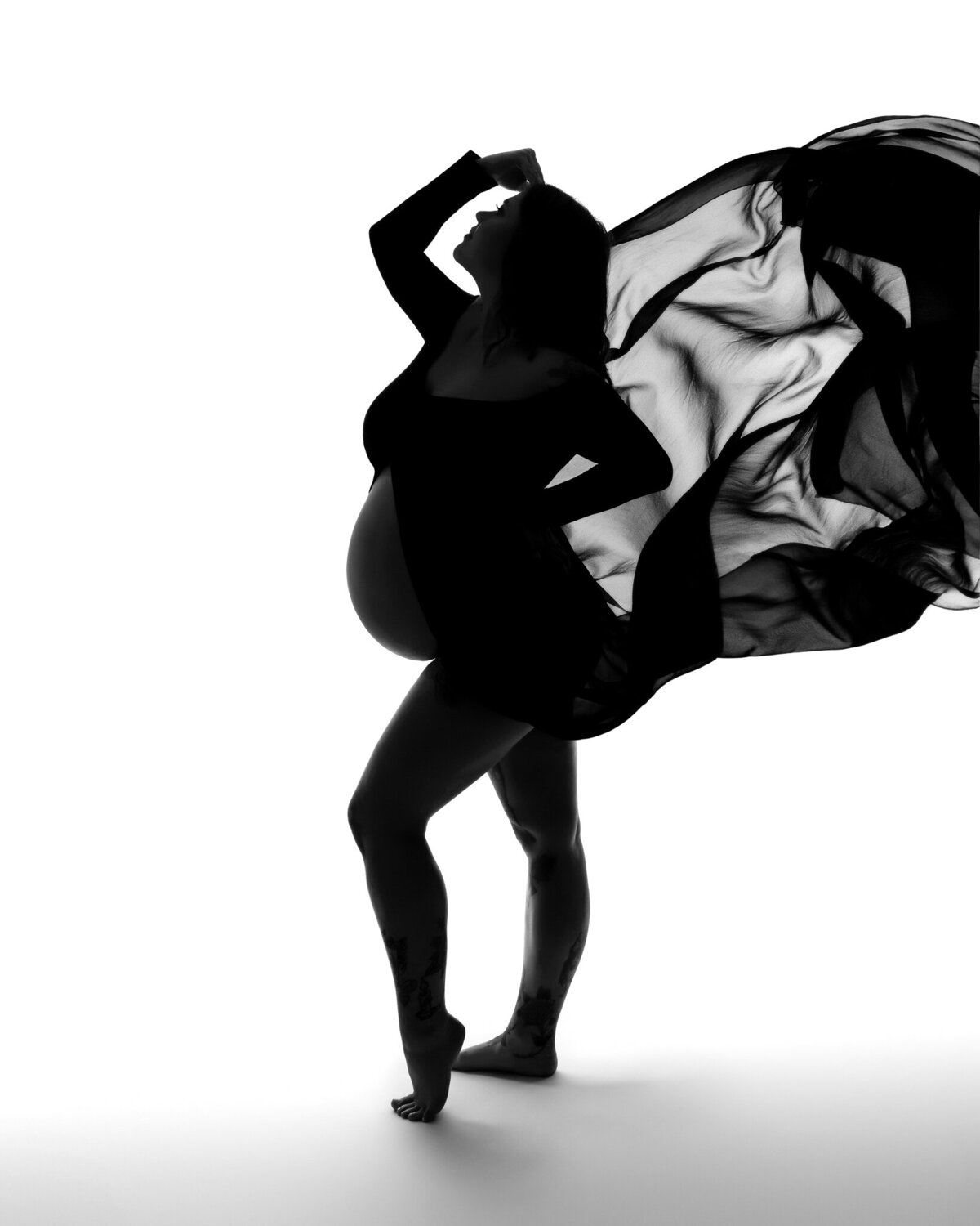 Backlit maternity silhouette with dramatic sheer black fabric captured mid-air, styled in Westlake.