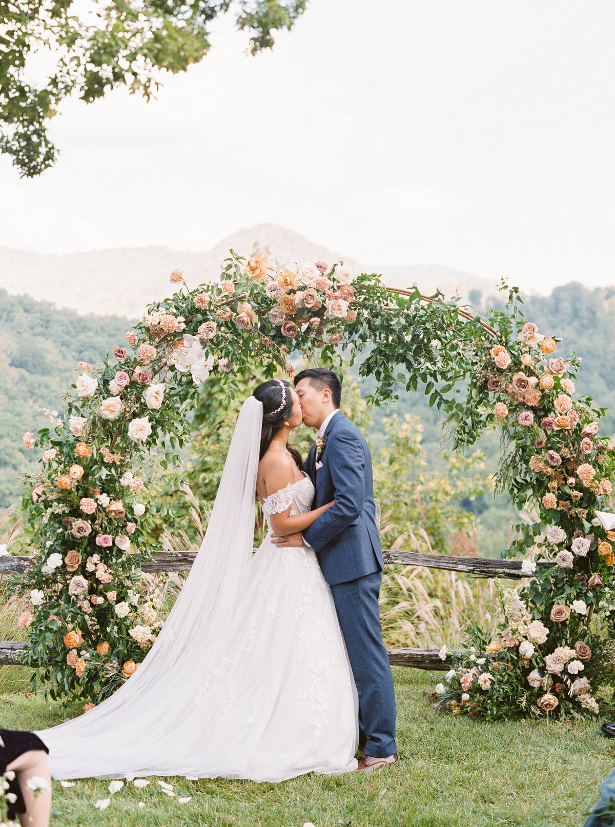 Bride and groom sharing their first kiss beneath a floral arch during mountain wedding ceremony at Castle Ladyhawke.