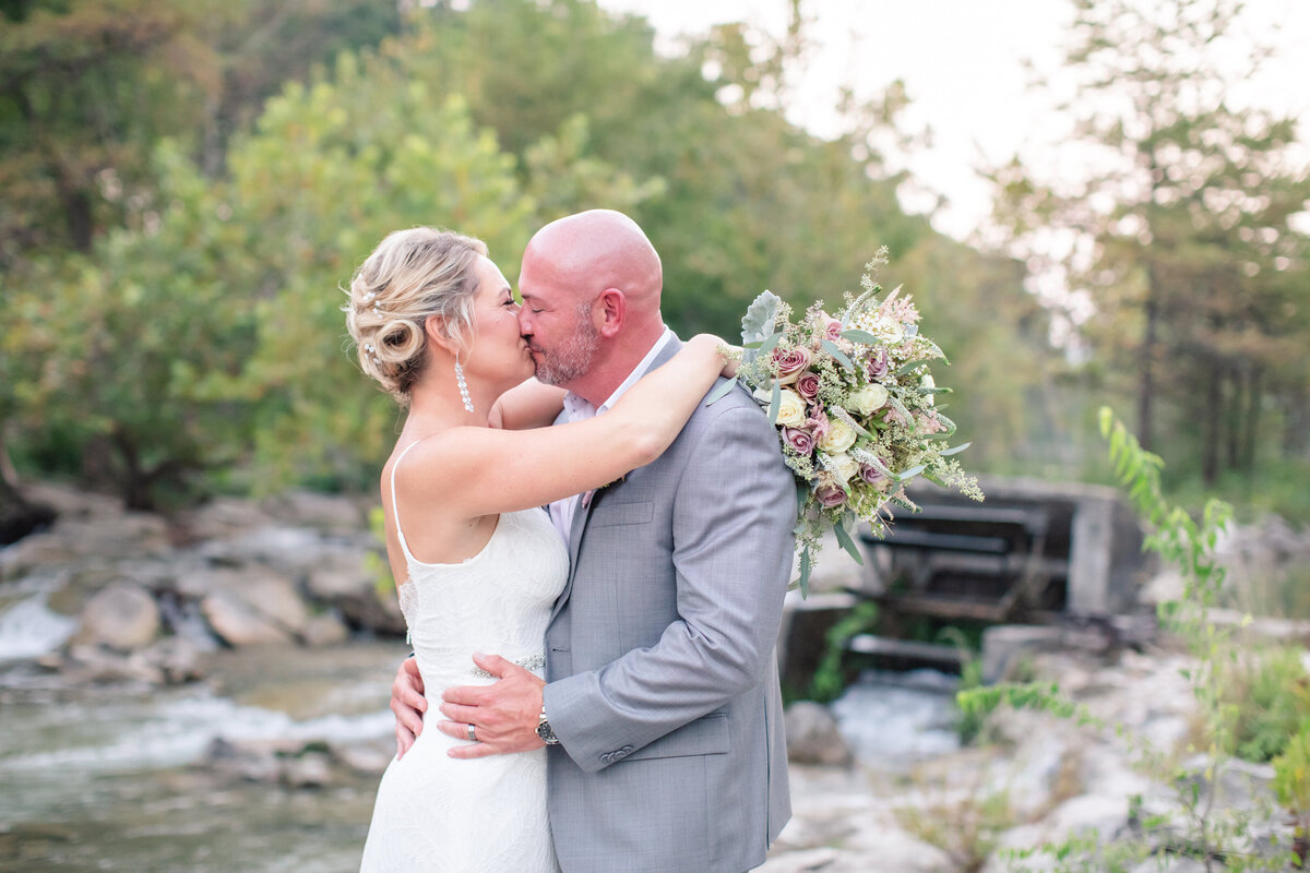 bride and groom kiss with water mill on river in background at New Braunfels wedding