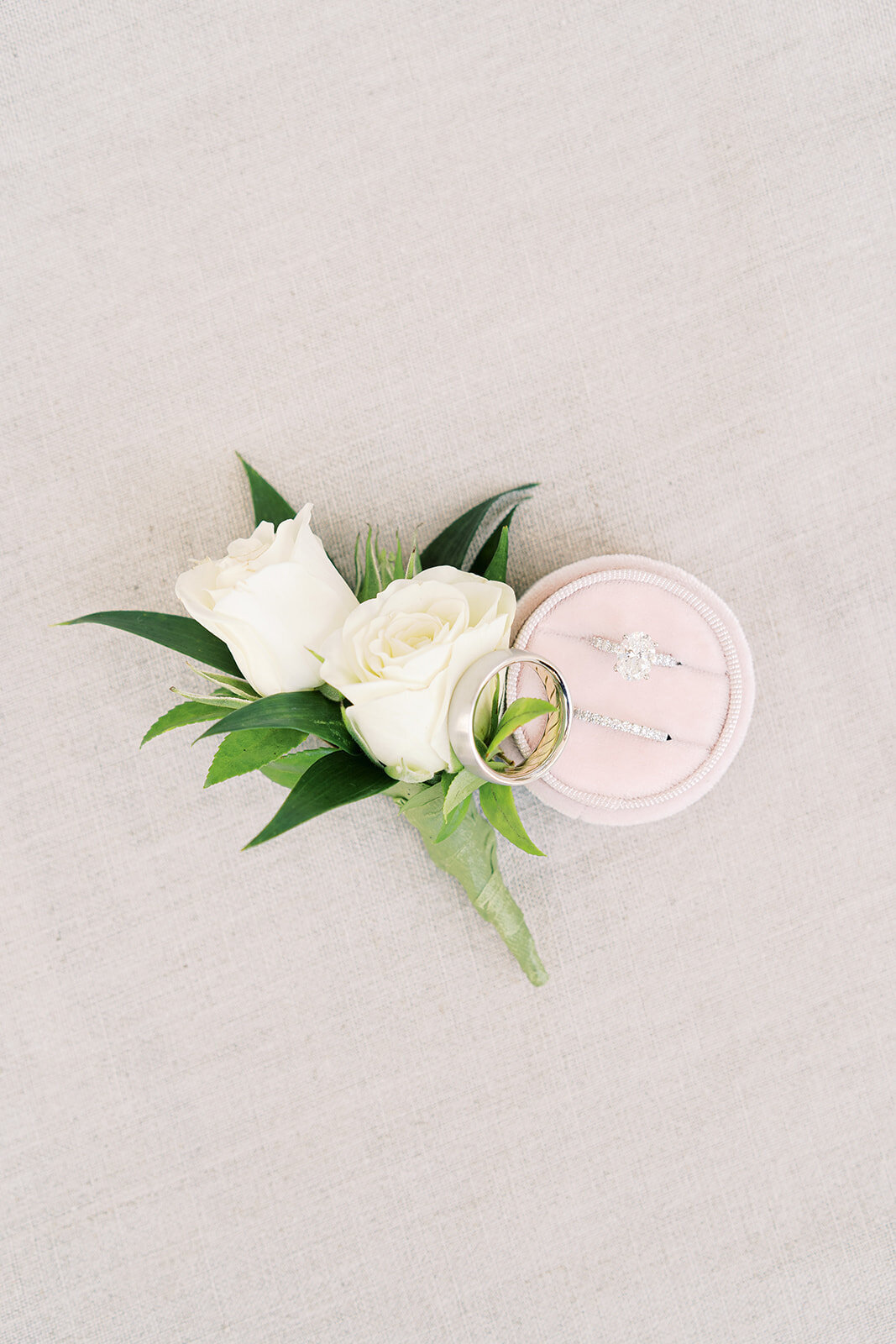 flat lay with white roses, wedding rings, and pink ring box
