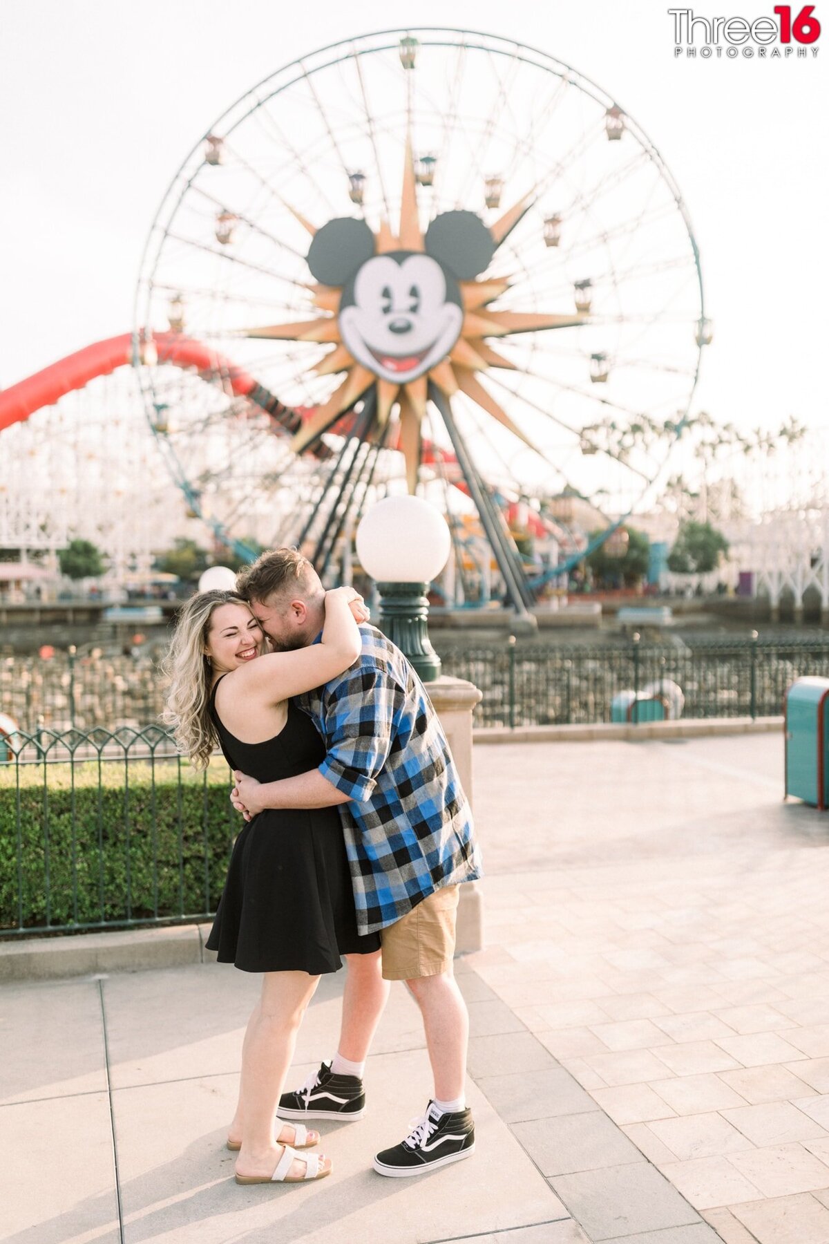 Soon to be married couple give each other a big hug with Mickey Mouse's roller coaster in the background.