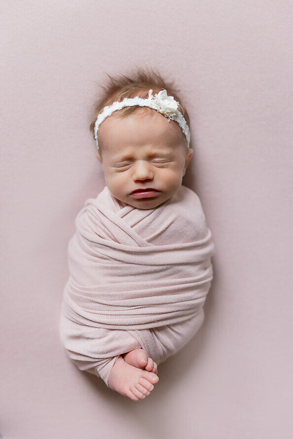 Newborn baby girl wrapped in pink on a pick backdrop.