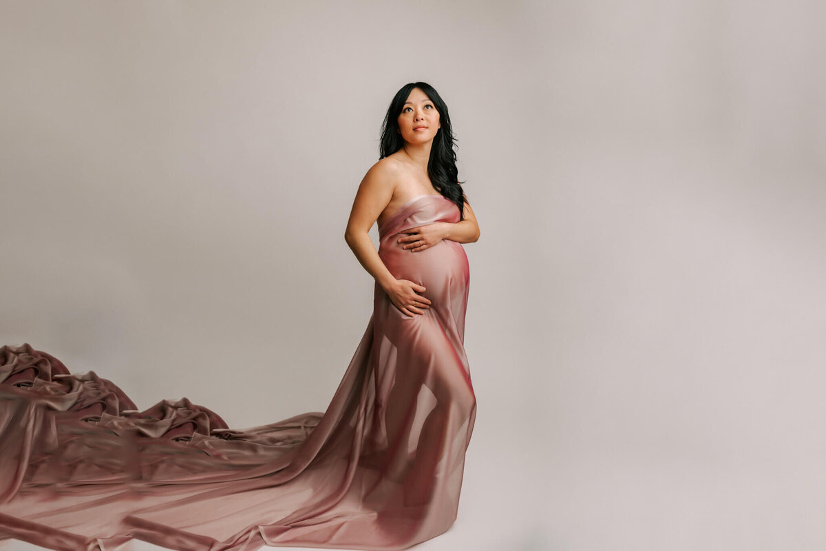 stunning maternity portrait of a mom draped in pink silk looking up and smiling