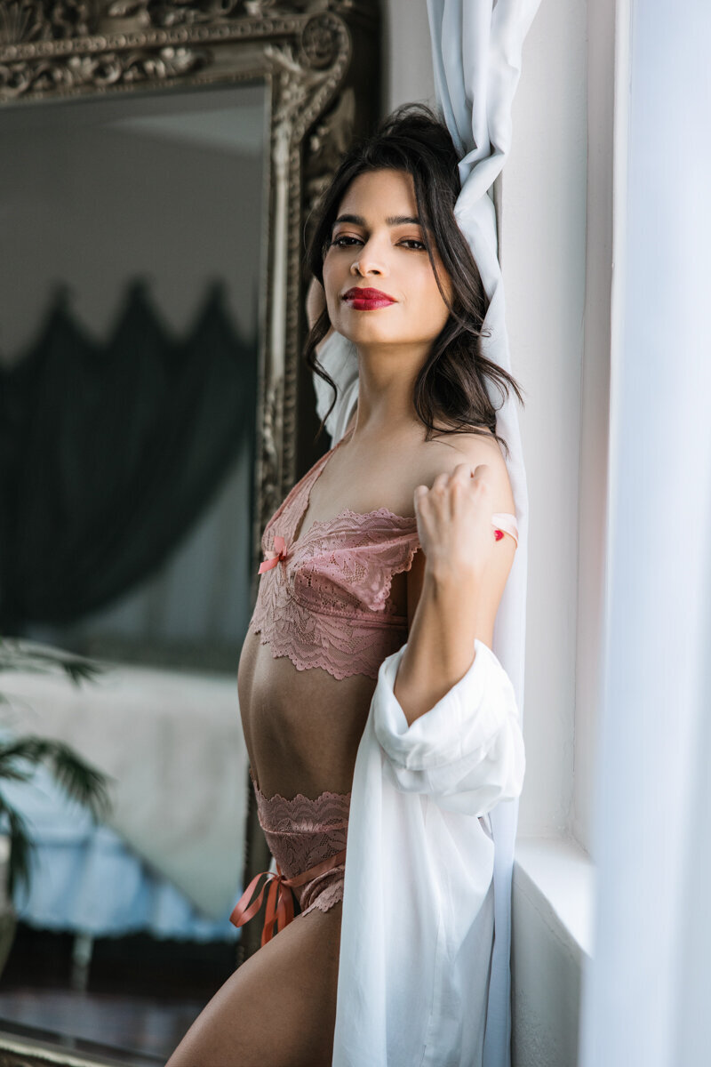 woman wearing pink lace bra panty and white sheer shirt against window