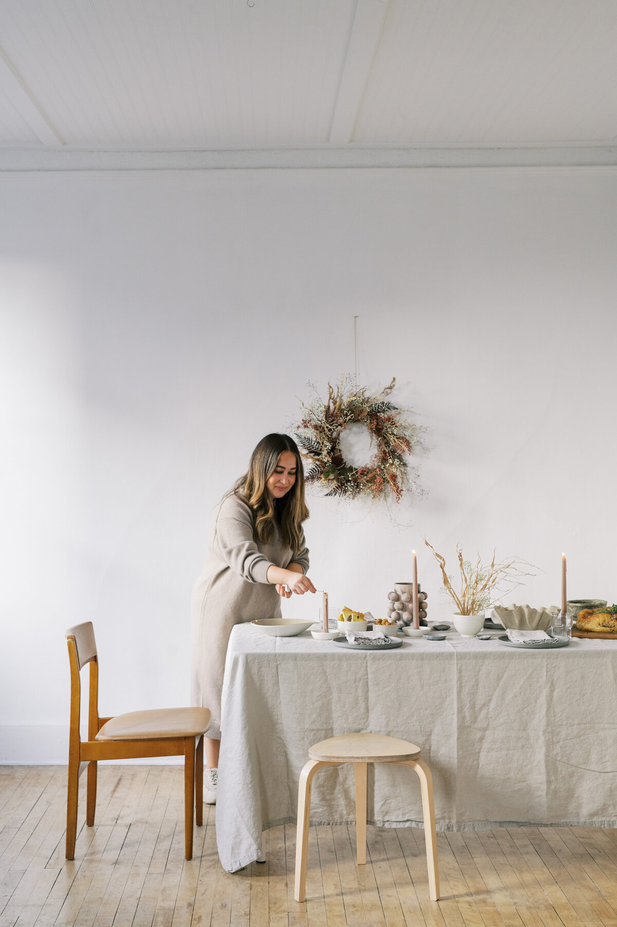 Woman wearing beige sweater dress lighting candles on neutral tablescape