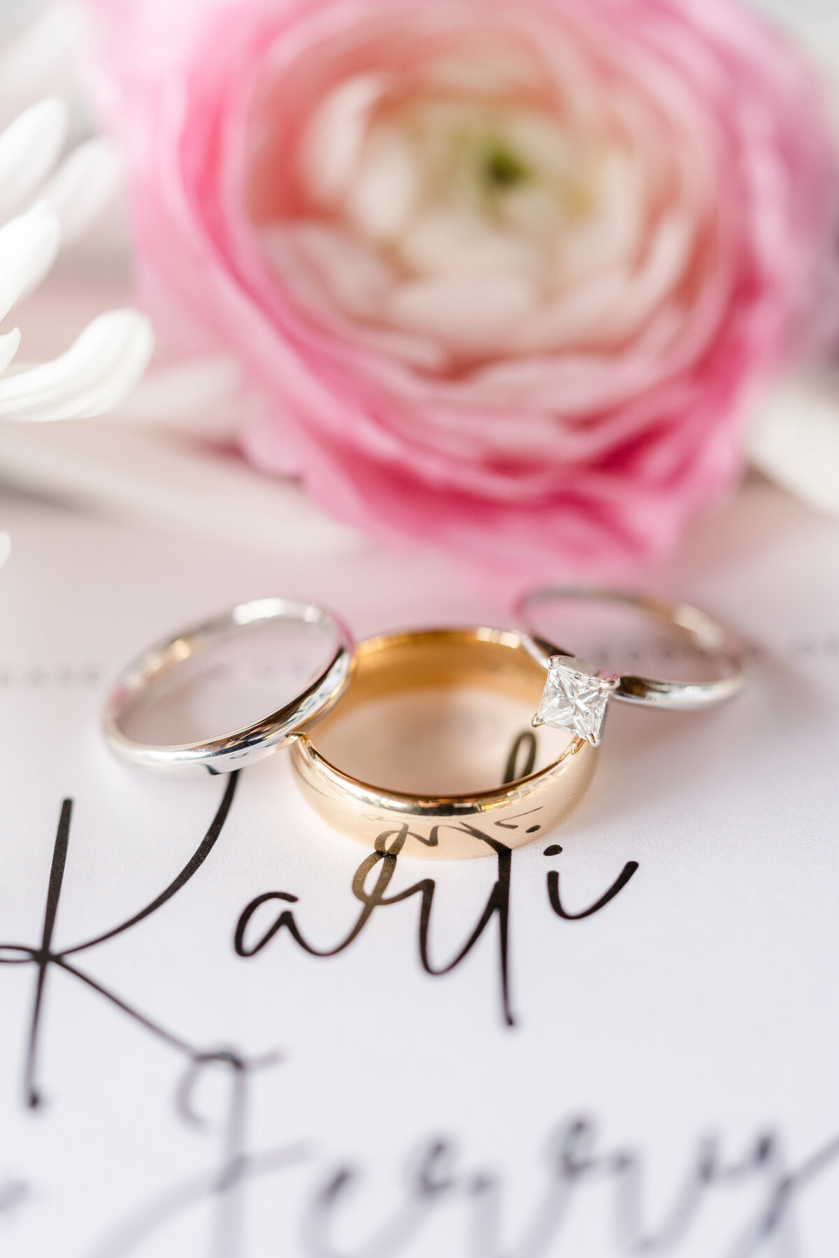 Wedding bands and engagement ring on wedding invitation with flowers in the background