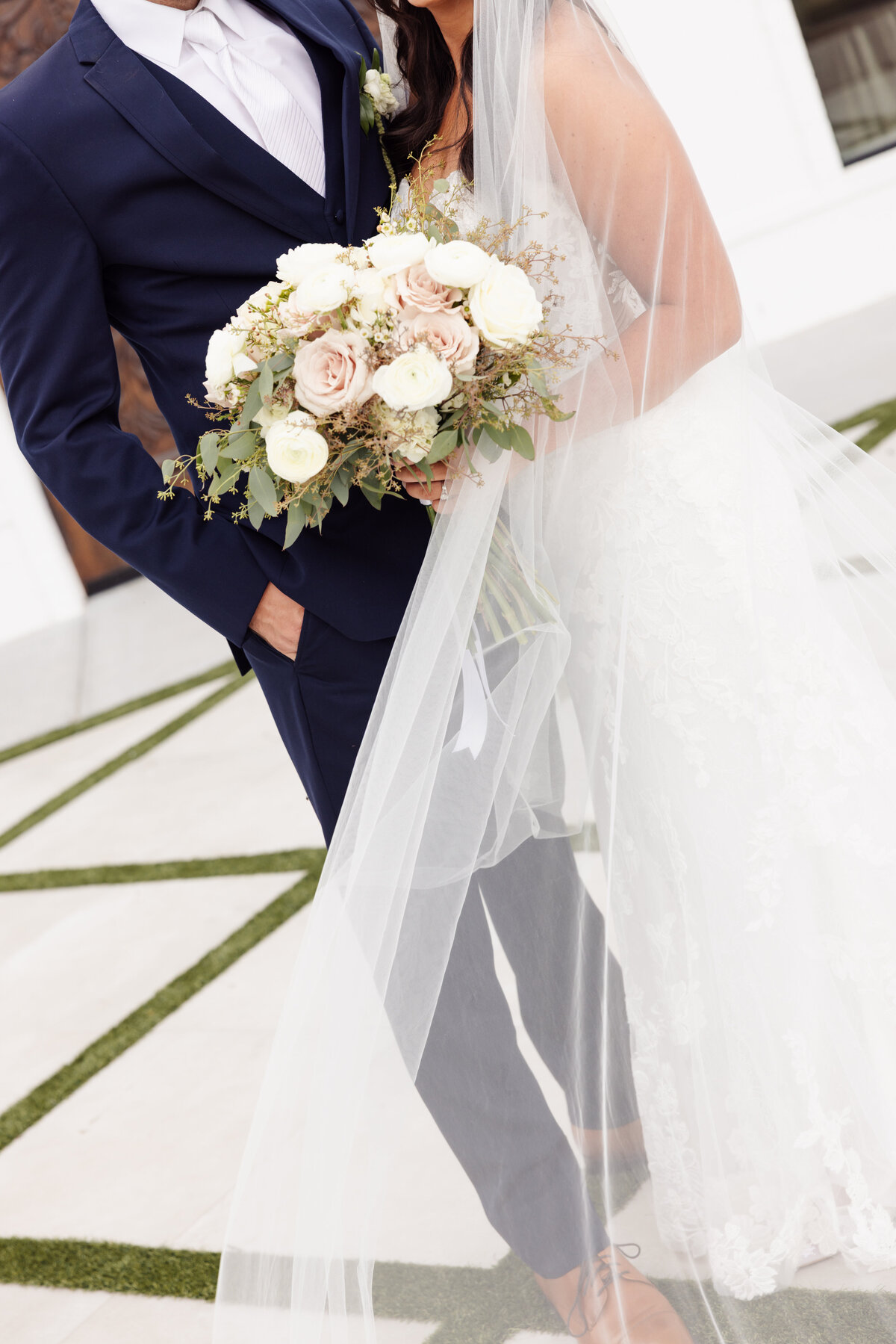 Close-Up of Bride and Groom Holding Bouquet Under Veil