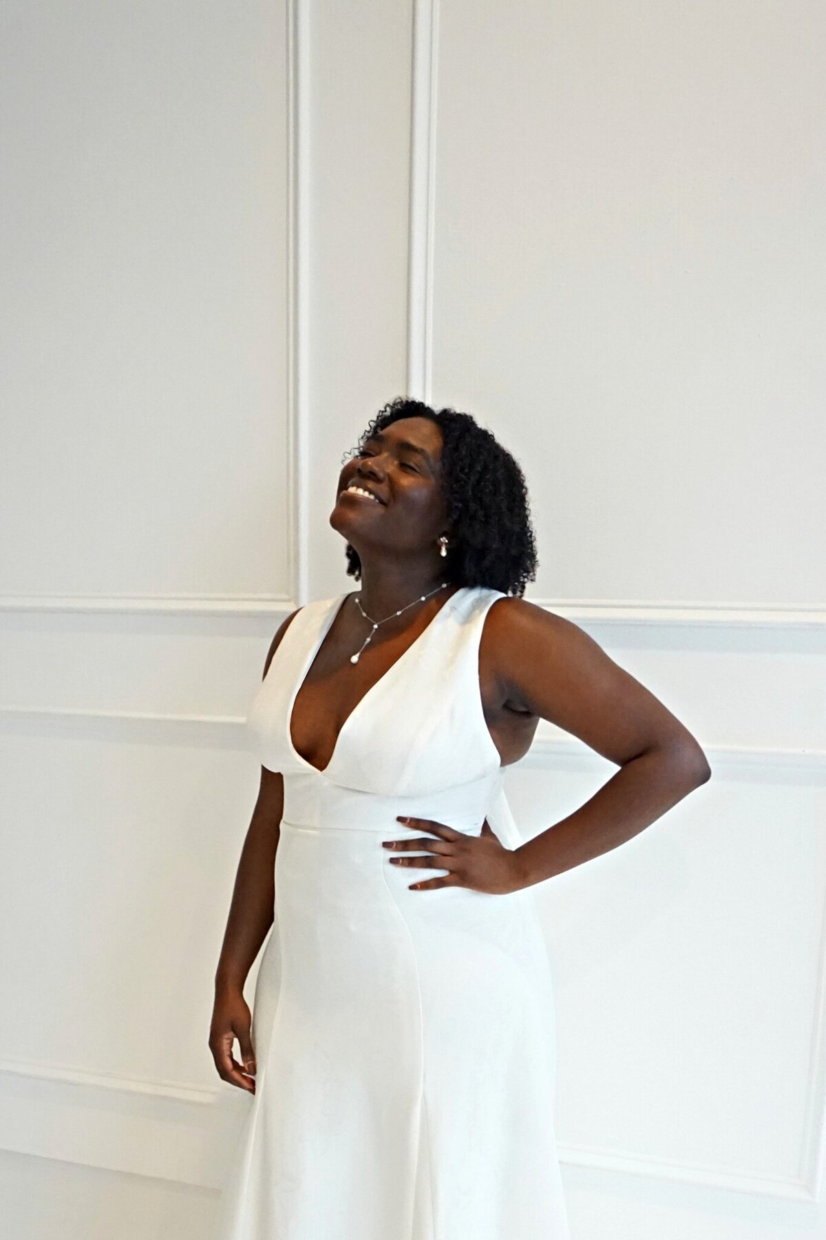 Close-up of a black model in the Sol v-neck wedding dress by Edith Elan paired with a pearl drop necklace by Ti Adoro.
