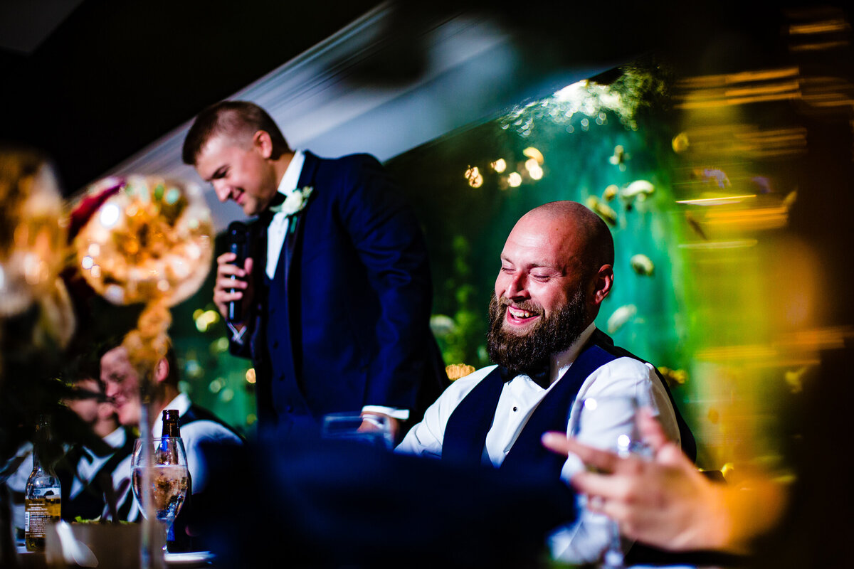 One of the top wedding photos of 2020. Taken by Adore Wedding Photography- Toledo, Ohio Wedding Photographers. This photo is of the best man giving a speech and the groom laughing. The wedding took place at the Toledo Zoo aquarium