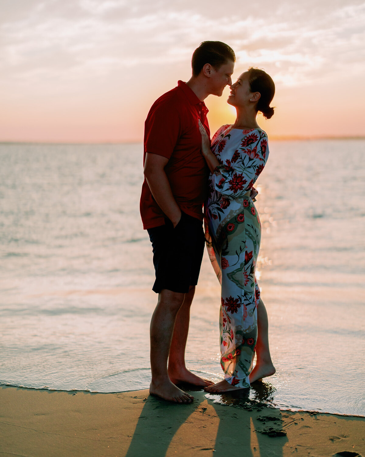 A couple standing nose to nose at the edge of the water at the beach 