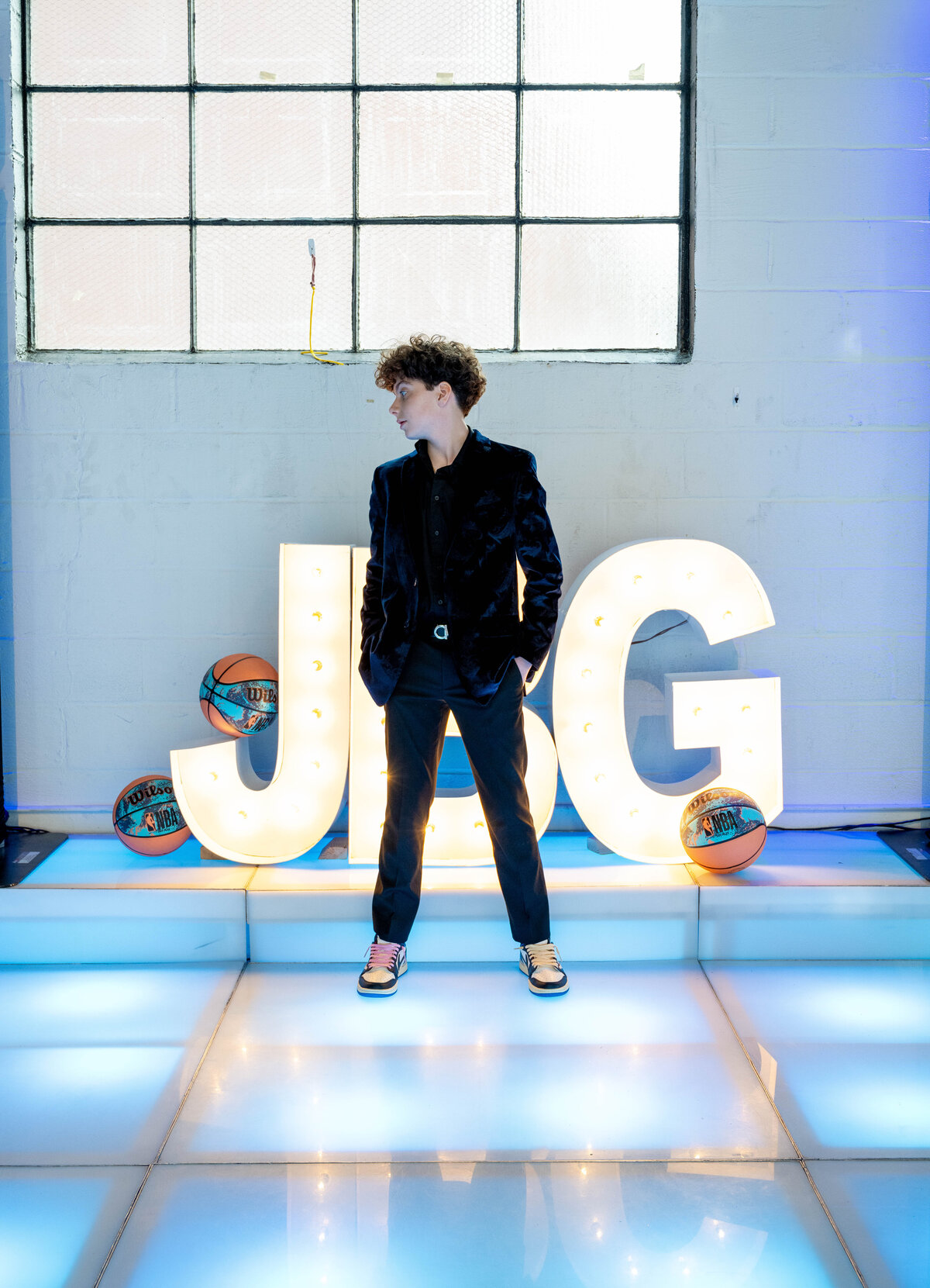 Guest of honor on custom light-up dance floor with initials and basketball-themed décor at a stylish bar mitzvah in Englewood Cliffs, New Jersey.

