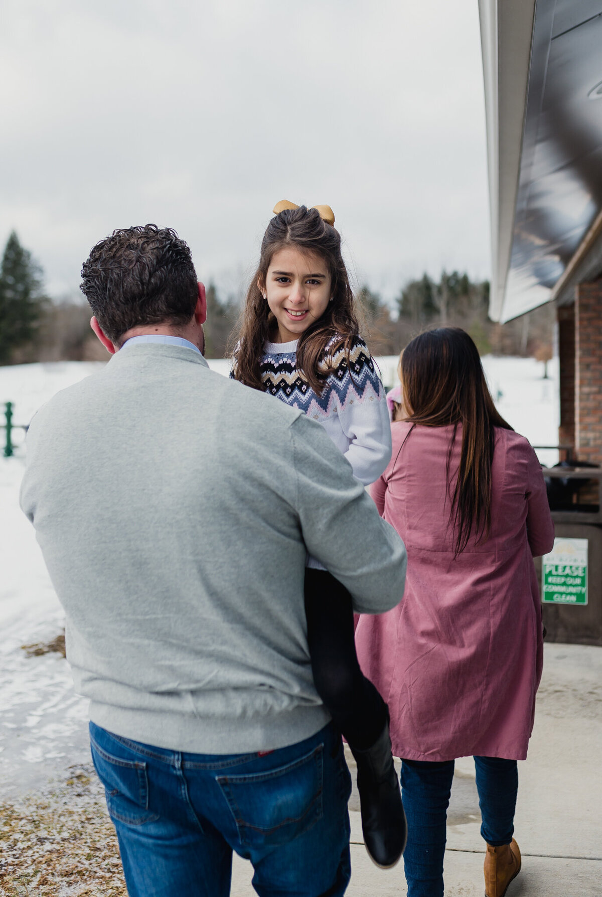 Dad holds girl while mom walks ahead.