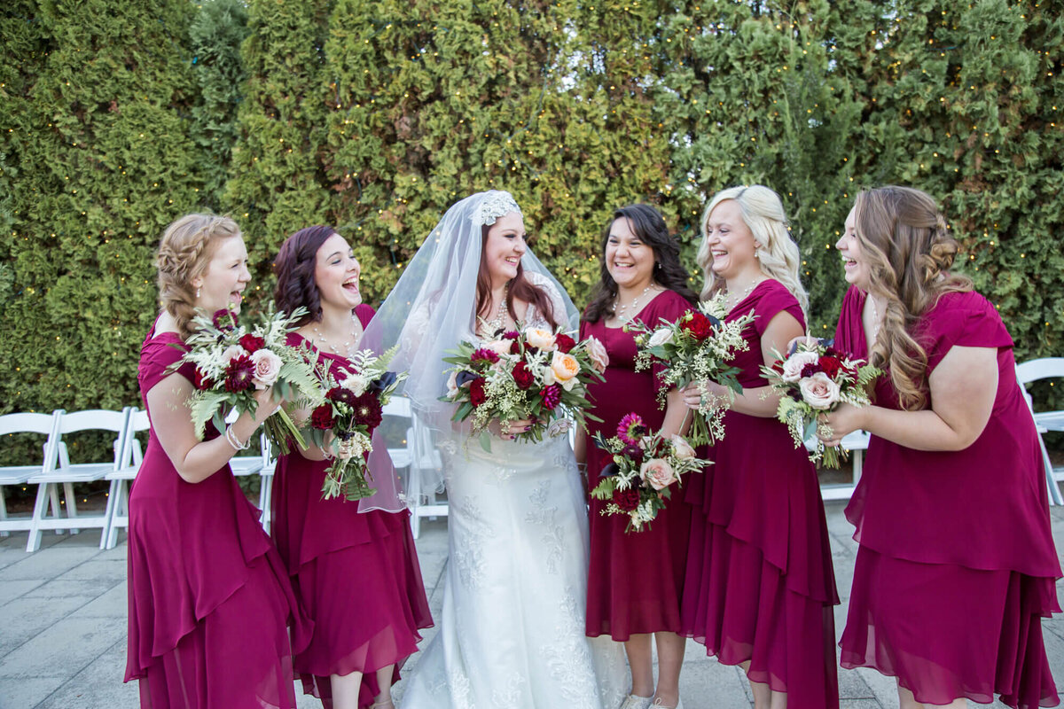 redheaded bride and her bridesmaids holding bouquets laughing with each other at beautiful garden wedding