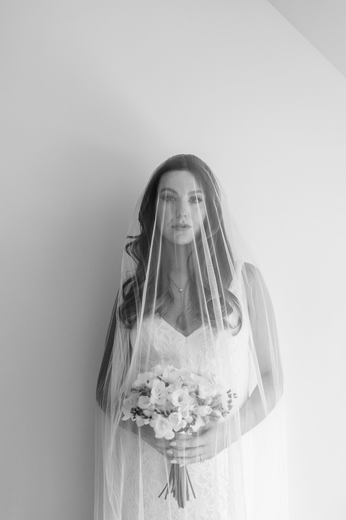 A dramatic black-and-white portrait of a pregnant bride holding a bouquet, her face elegantly framed by a delicate bridal veil