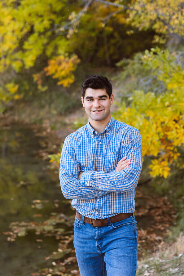 Senior boy crosses his arms in front of fall leaves at Fly N B park.
