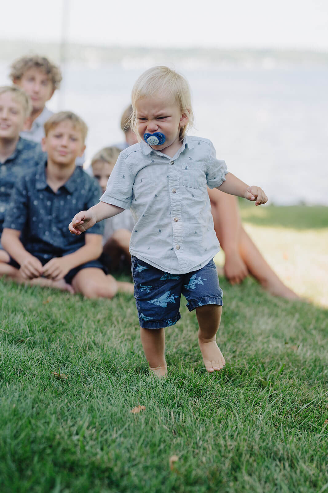 toddler walking on grass with family looking on at generational photoshoot in Finger Lakes, NY