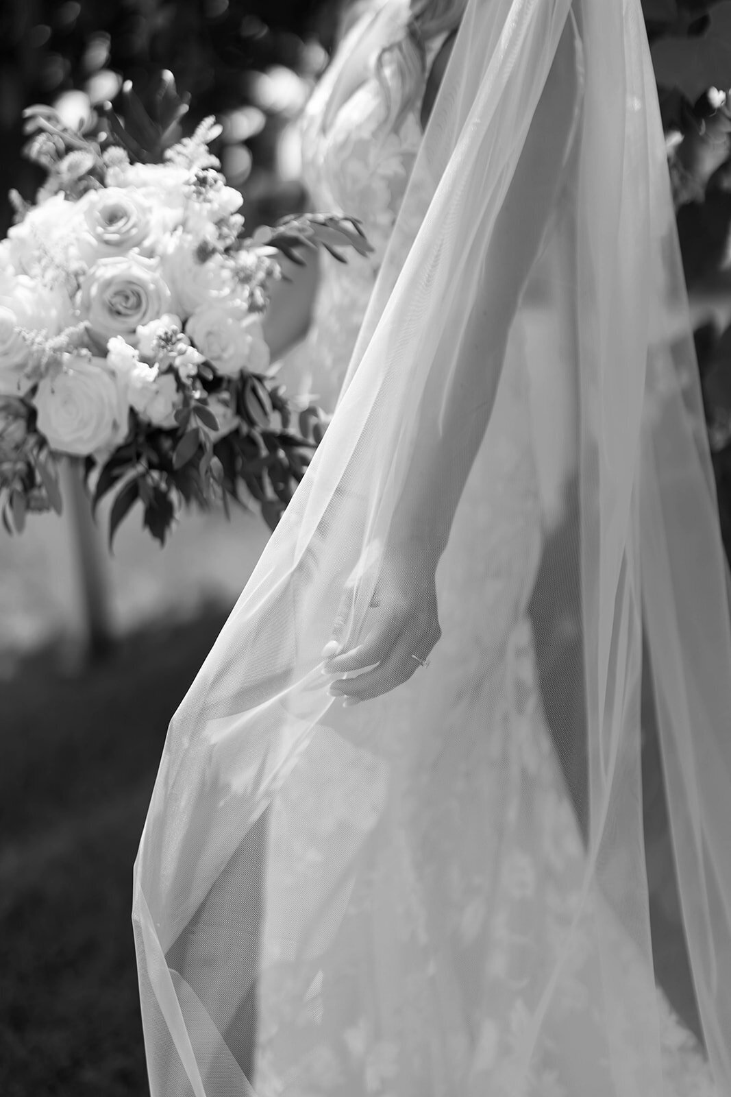 black and white photo of bride holding veil and bouquet outside at windridge estate wedding venue