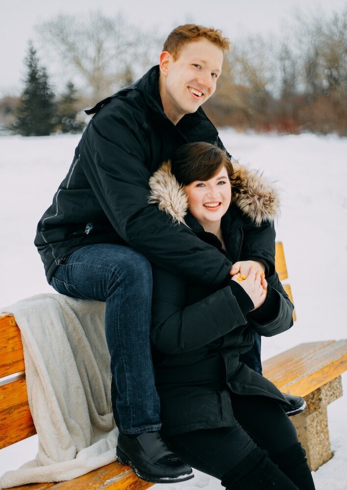 Woman sits on a bench with husband sitting behind her