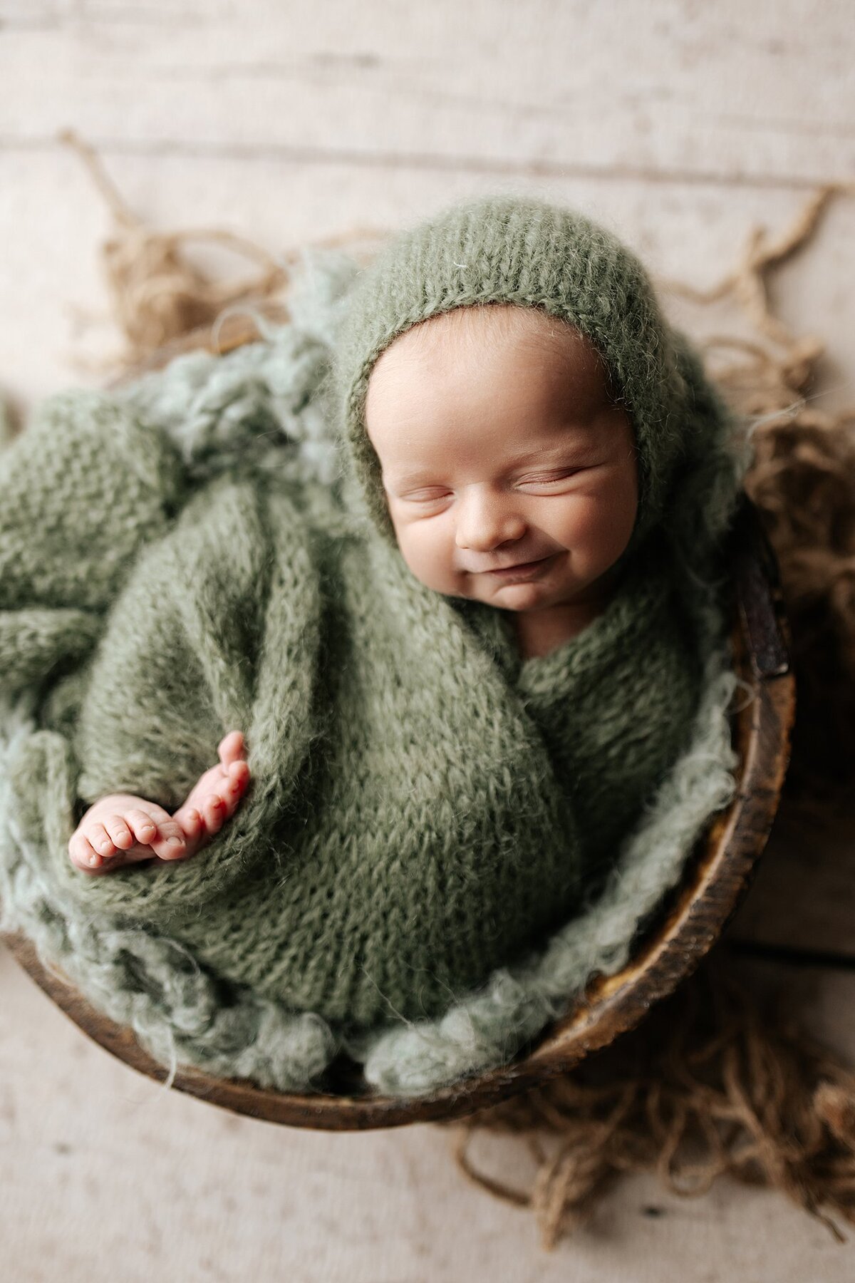 Newborn baby boy grinning in a round basket in a newborn studio in Springville alabama photography studio lit