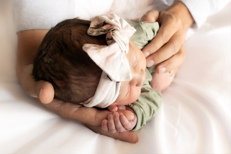 Newborn baby resting in dad's hands holding onto one of dad's fingers.