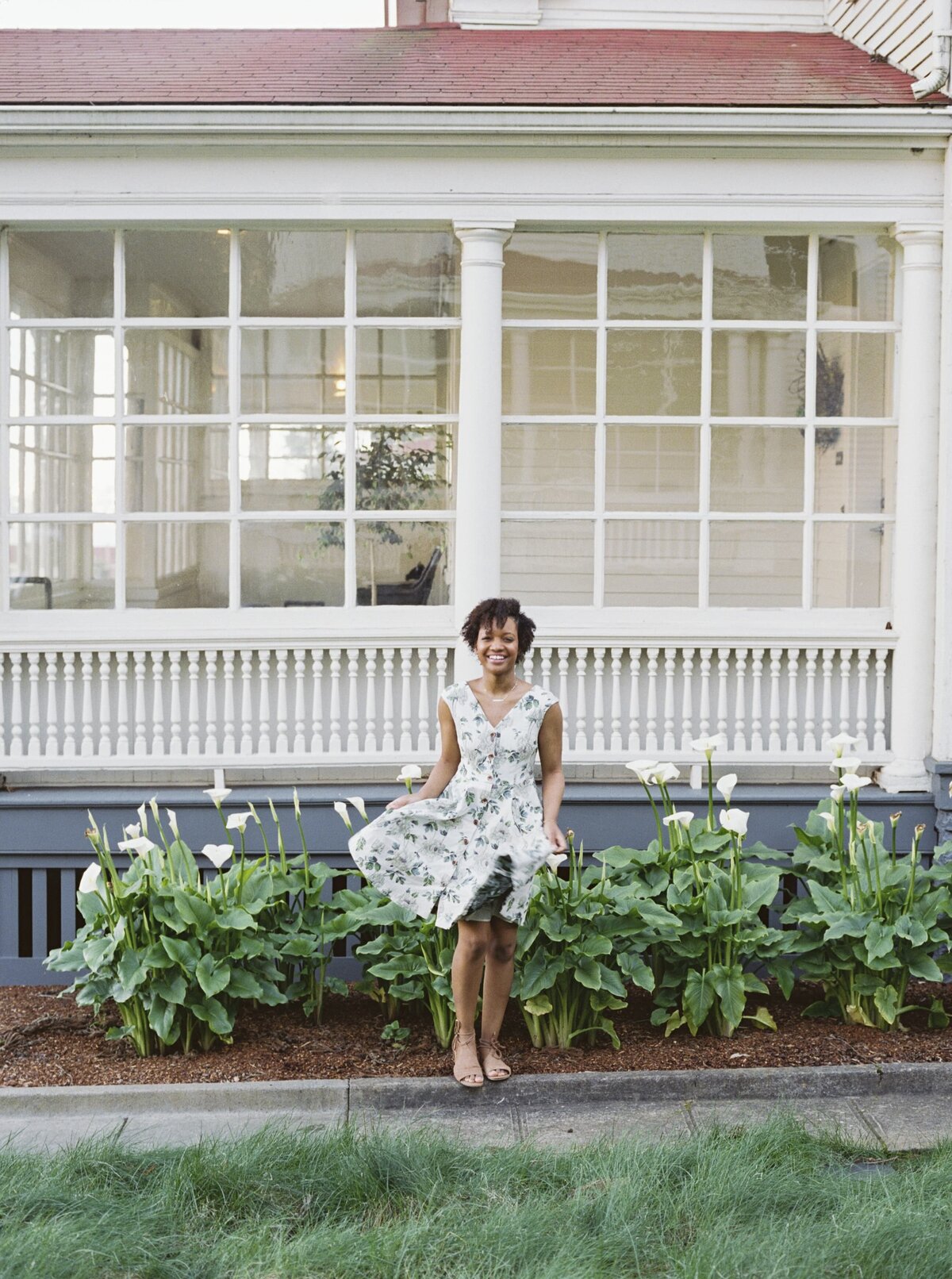 Woman standing in front of a white home with lots of windows and greenery