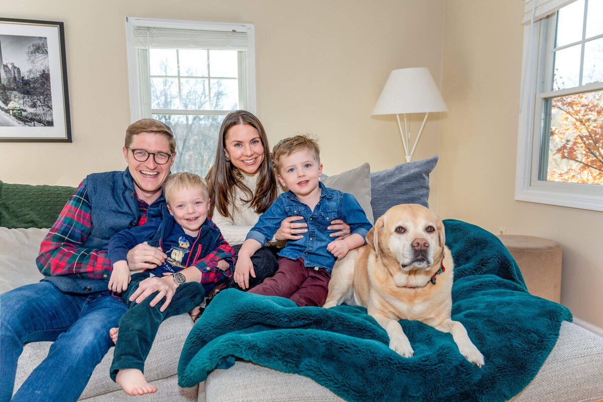 Sweet family cuddled on the couch with their two toddler boys and a yellow lab during an at-home session in Weston, CT.