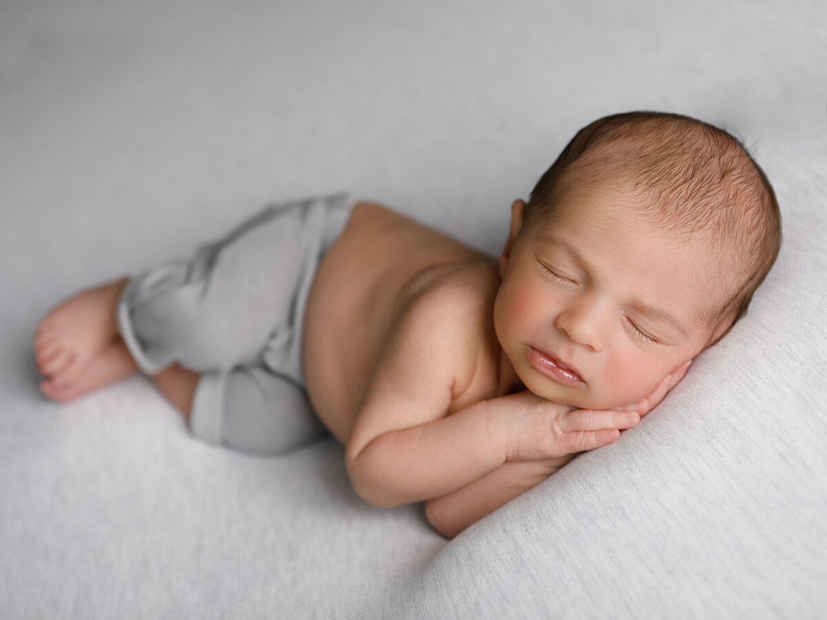 Newborn-photography-session-newborn-sleeping-on-his-side-on-grey-blanket-and-pants,-photo-taken-by-Janina-Botha-photographer-in-Oakville-Ontario
