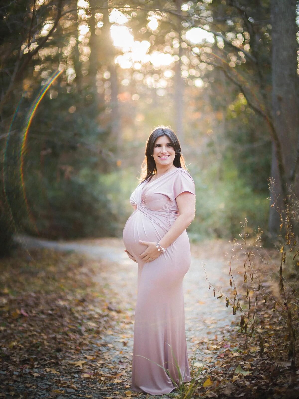 A pregnant woman holding the bottom of her stomach and smiling.
