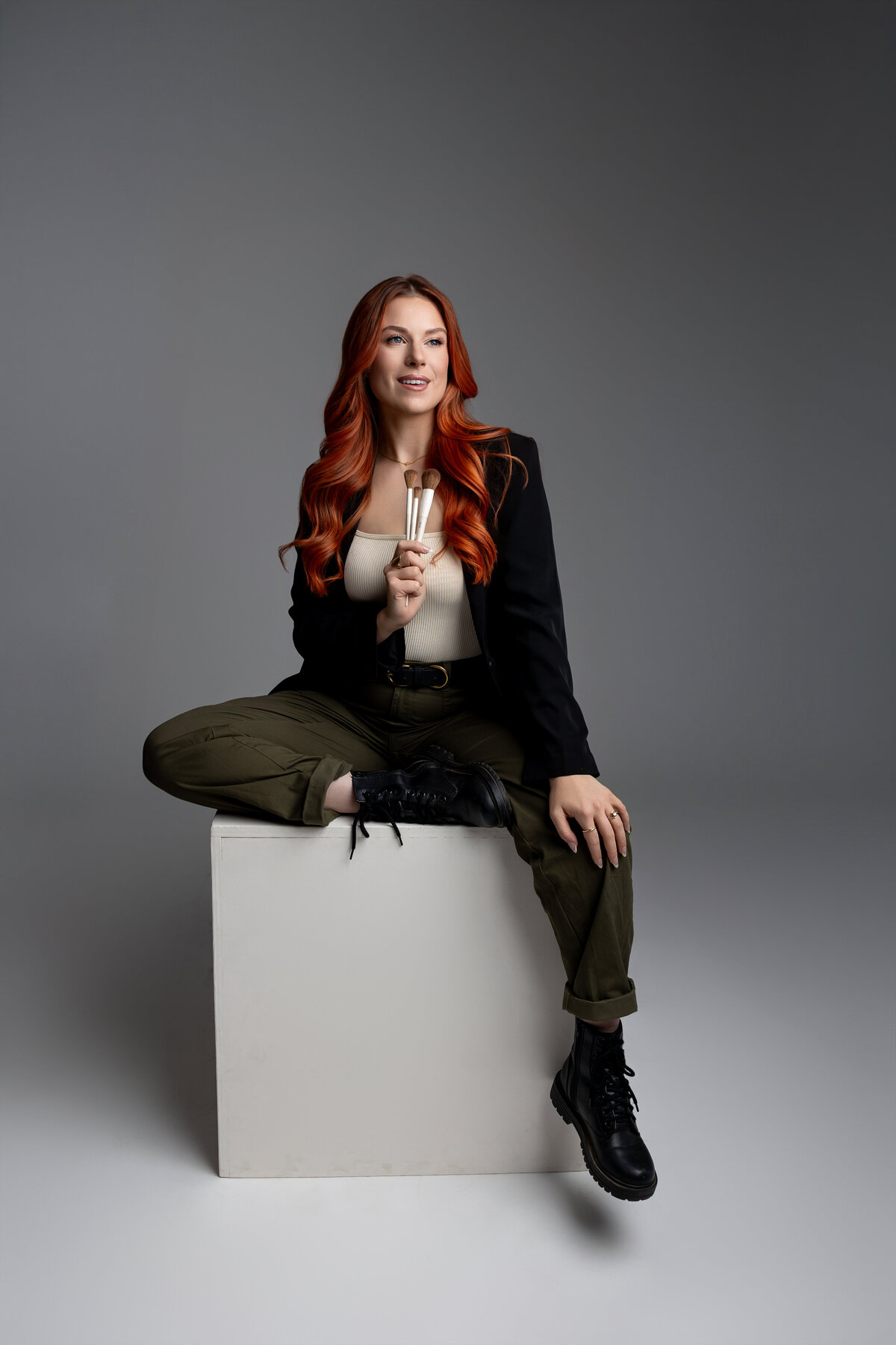 Red-haired woman seated on stool with legs crossed for studio branding portrait. Photograph by Yucaipa branding photographer Kaitlyn Dawn Photography.