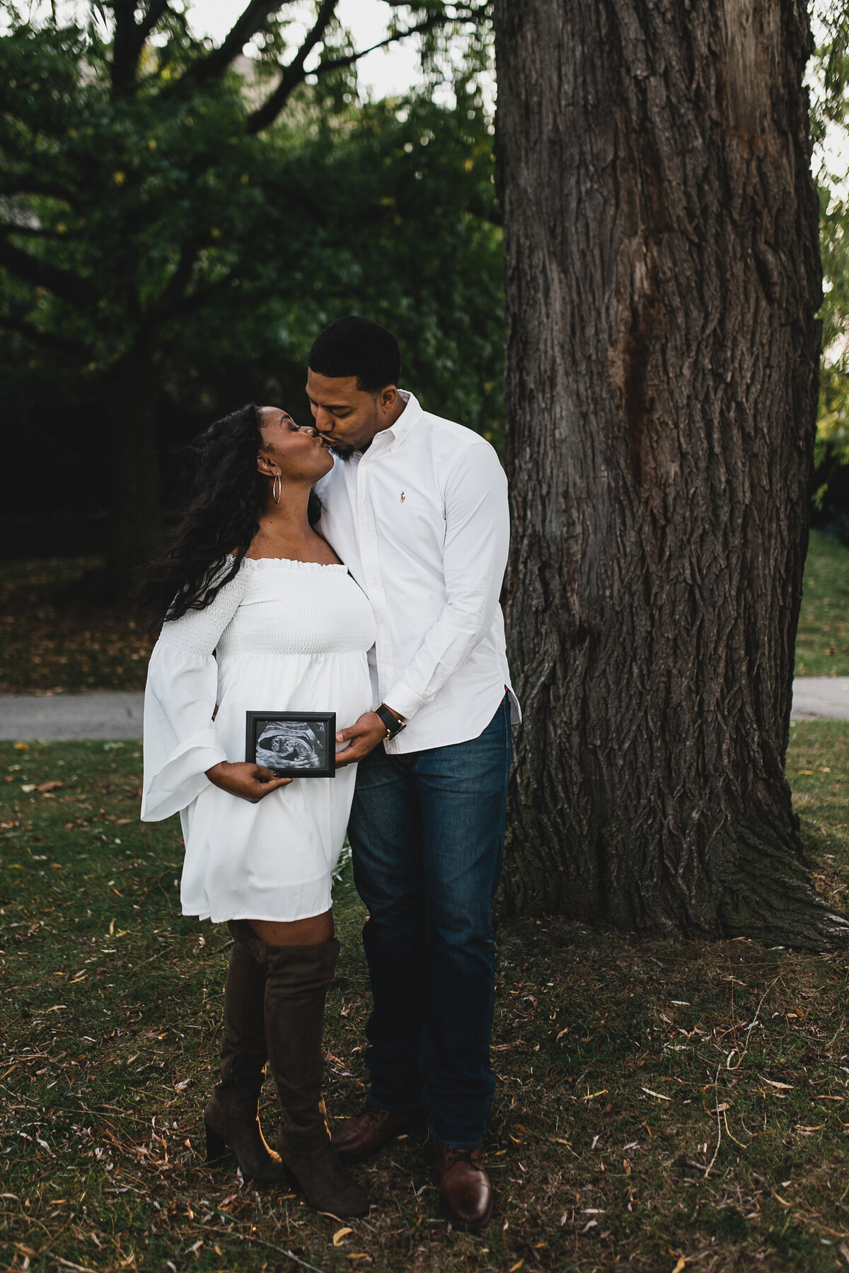 Maternity photography of a woman holding ultra sound and kissing a man outside.