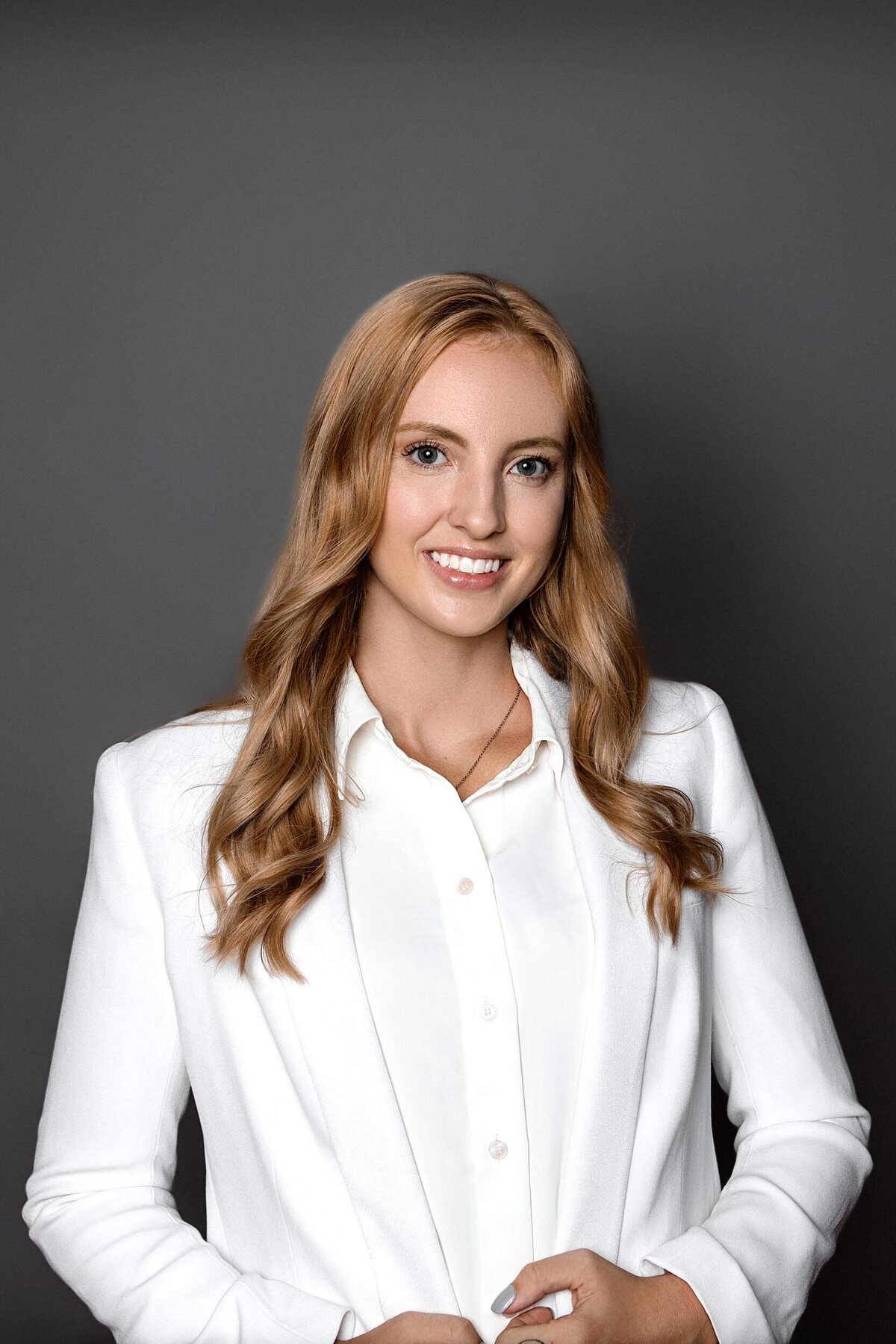 Real Estate Headshot of a woman wearing a white suit on a dark gray background smiling at the camera