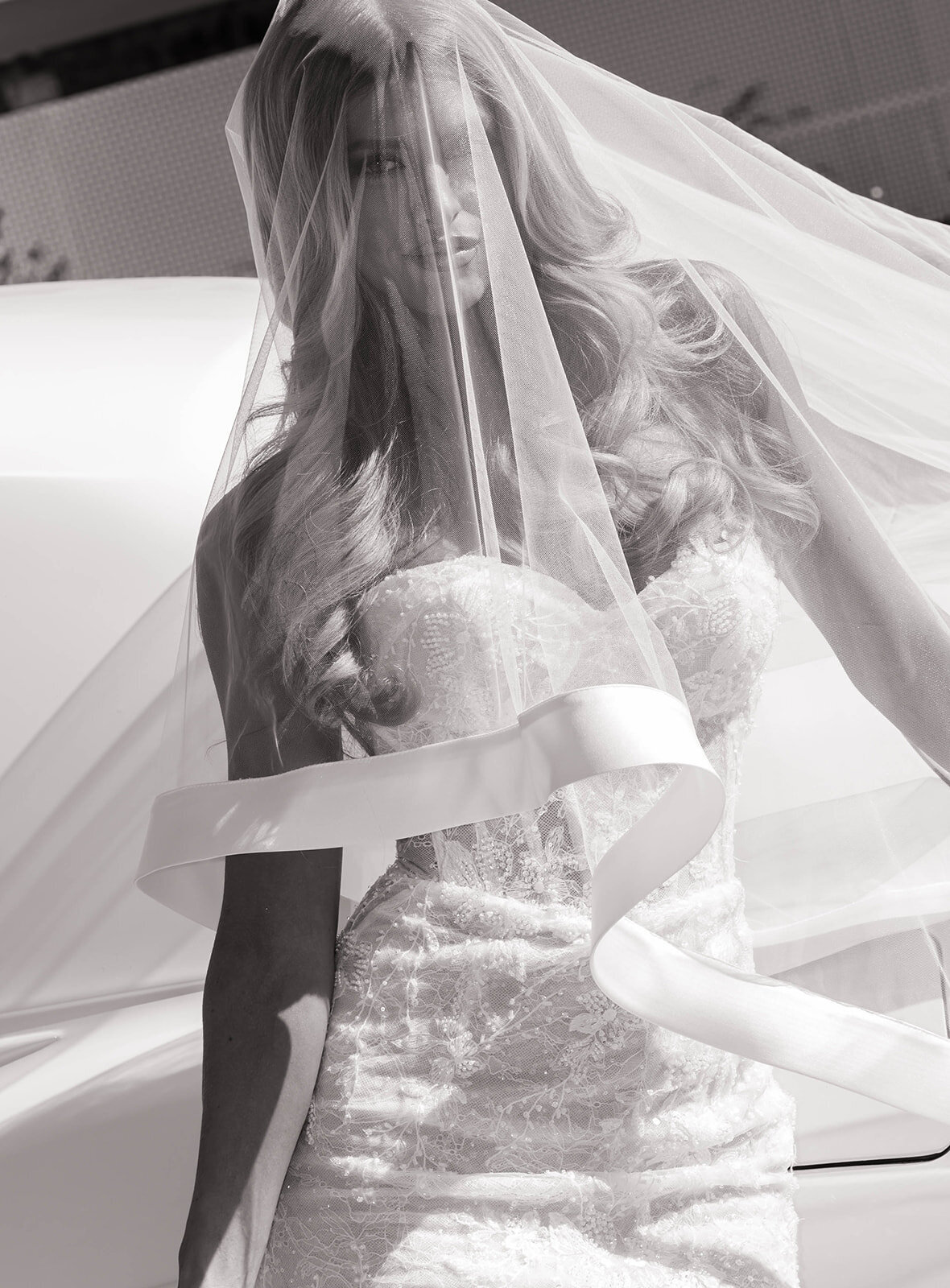 A bride and groom walk hand in hand outdoors, smiling at each other. She holds a colorful bouquet, wearing a white gown, while he is in a beige suit.