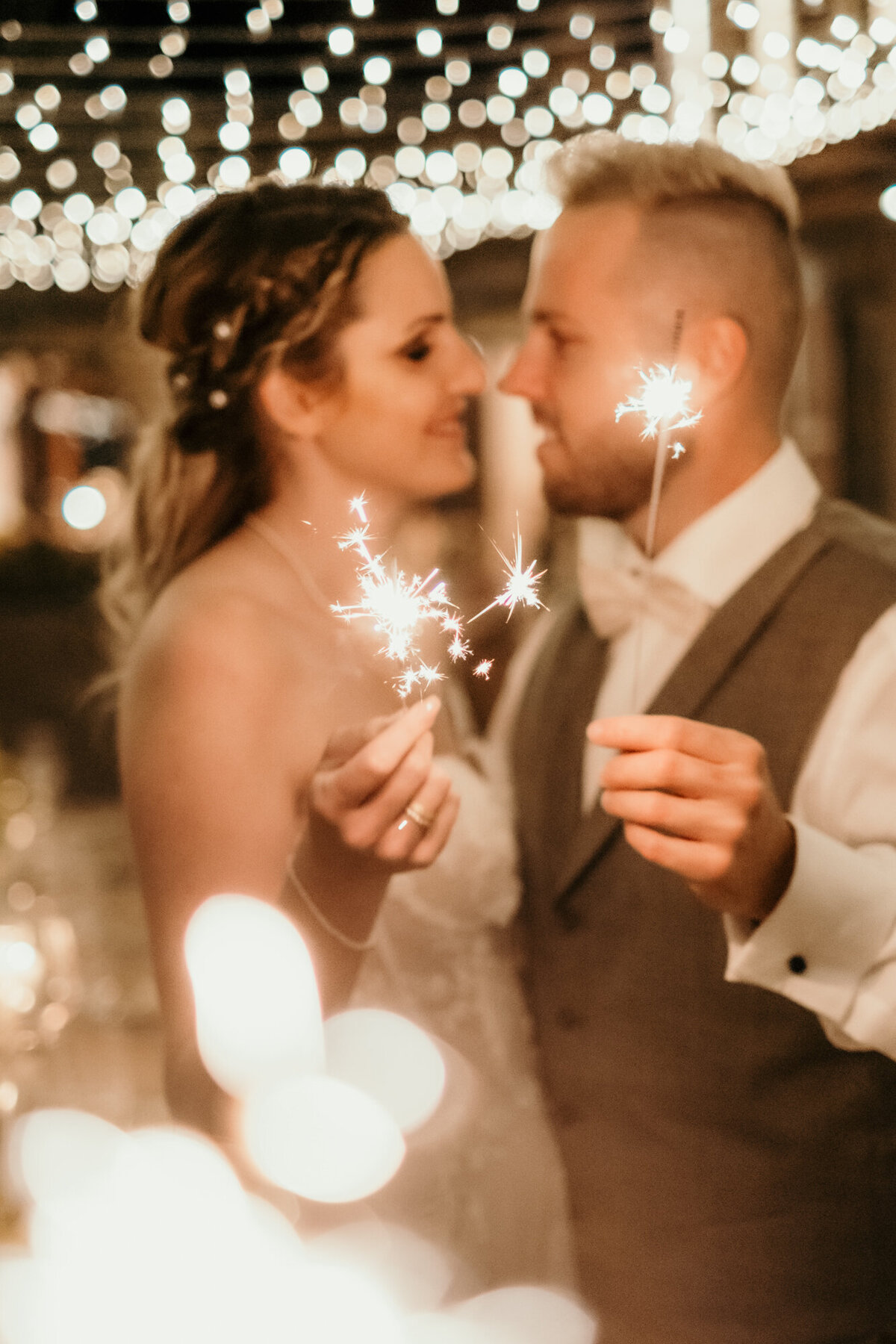 Verliebt blickt sich das Hochzeitspaar umgeben von Lichtern tief in die Augen und hält Wunderkerzen.