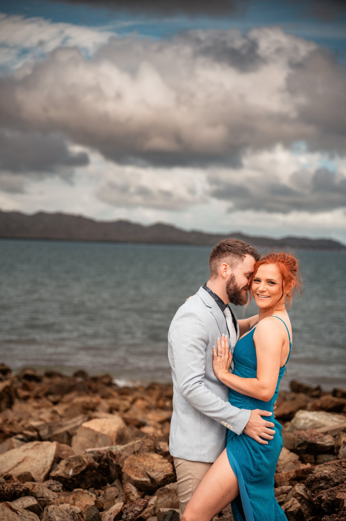 ma in suit and woman in blue split dress on a beach in Townsville  in a loving embrace - Townsville Engagement Photography by Jamie Simmons